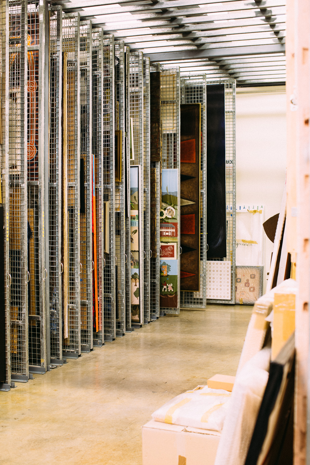 Paintings hang on wire racks in an artwork collection storeroom